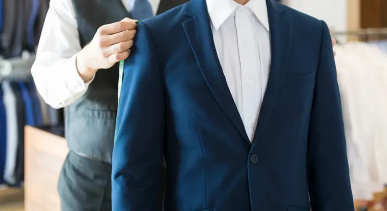 A tailor measuring the shoulder of a navy suit jacket